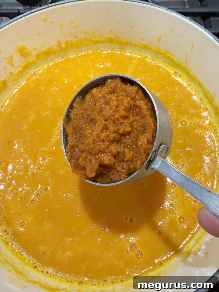 Adding pumpkin puree to the soup pot.