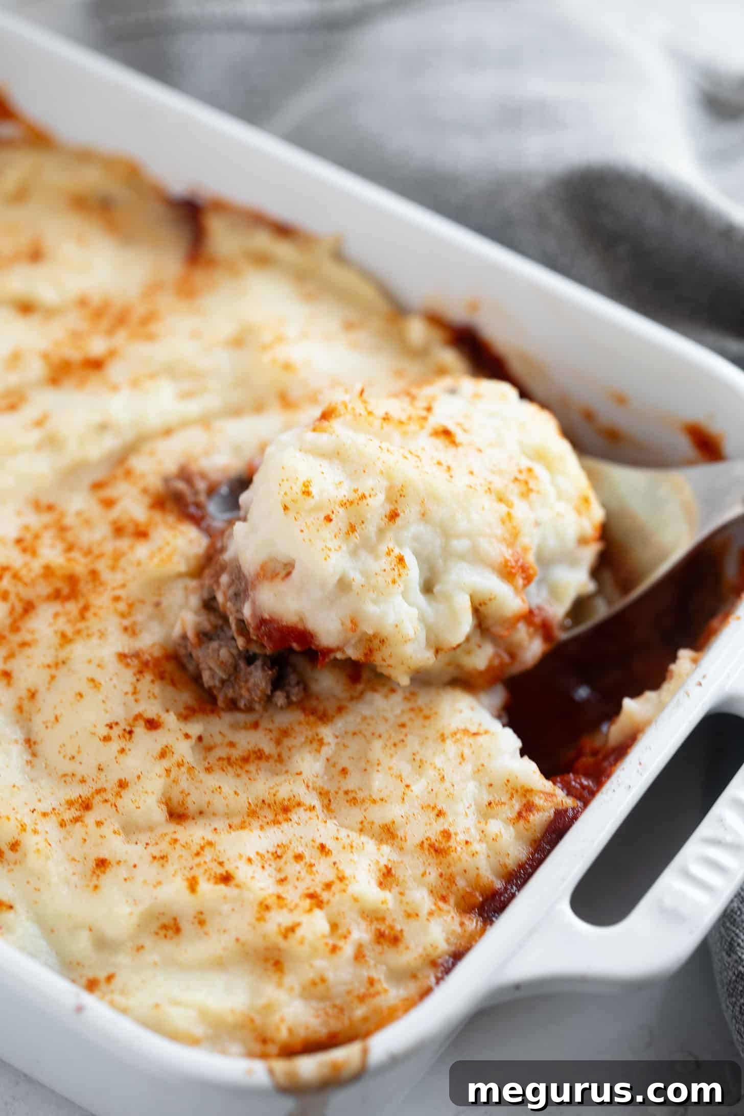 Close-up of a slice of meatloaf casserole, showing distinct layers of meat, sauce, and potatoes.