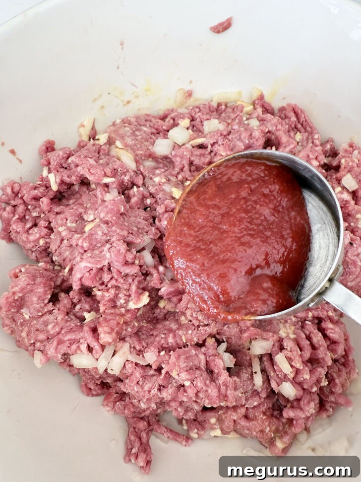 Adding tomato sauce to the meat mixture to infuse flavor.