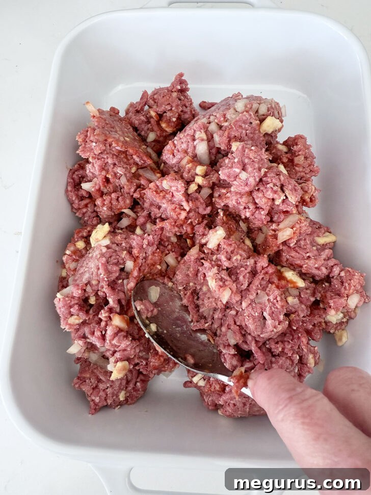 Pressing the meat mixture firmly into a casserole dish for an even base.