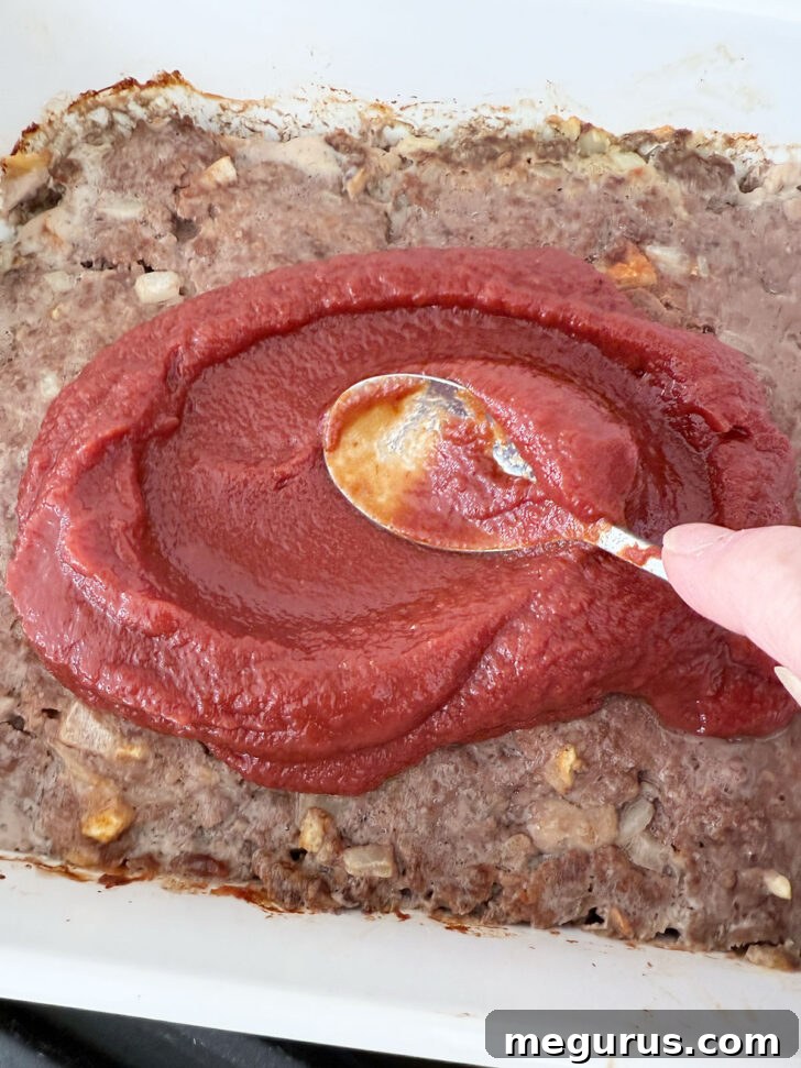 Spreading the rich tomato sauce over the pre-baked meatloaf layer.