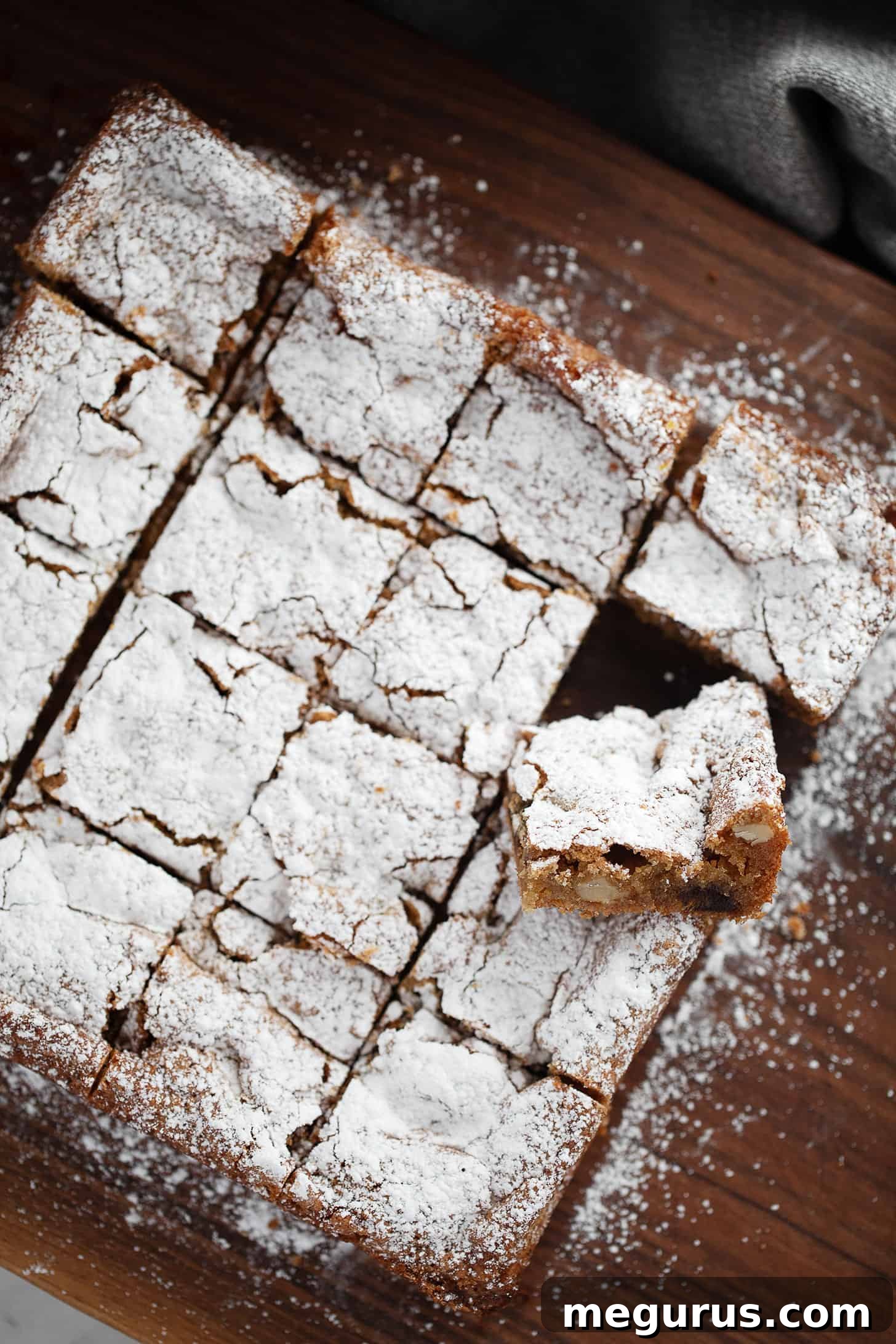 A close-up of beautifully cut date and nut chews on a cutting board, dusted with powdered sugar.