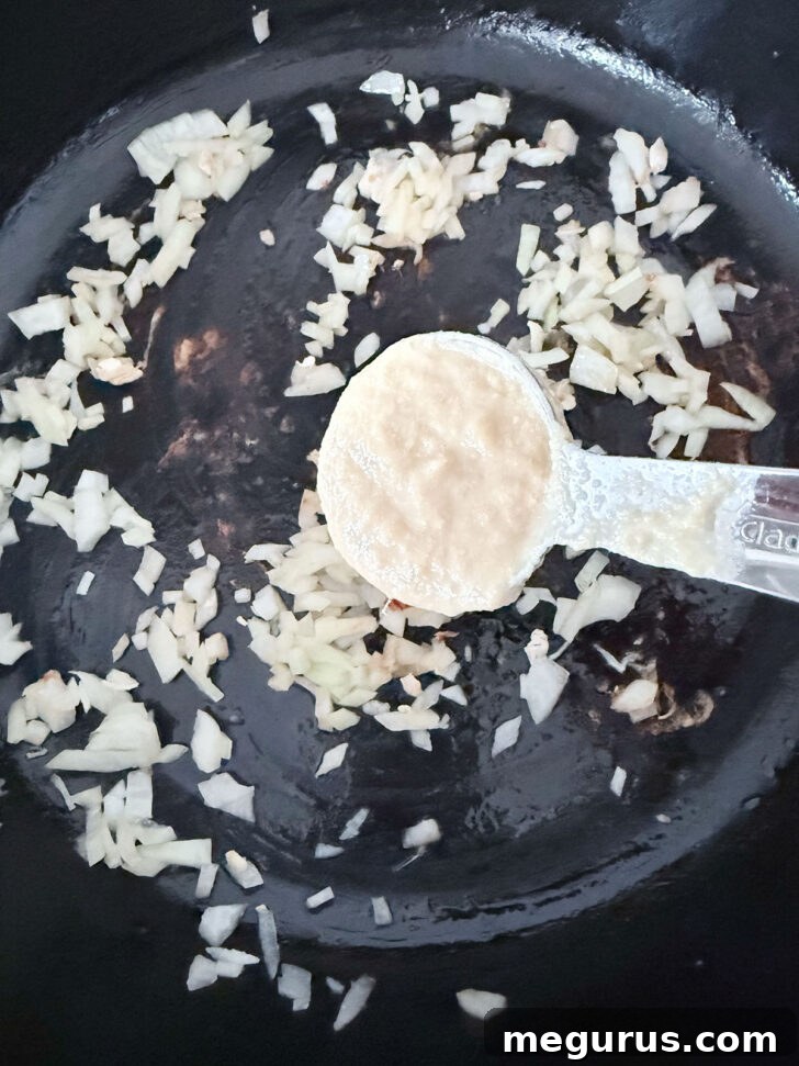 Adding ginger garlic paste to the skillet with the onion.