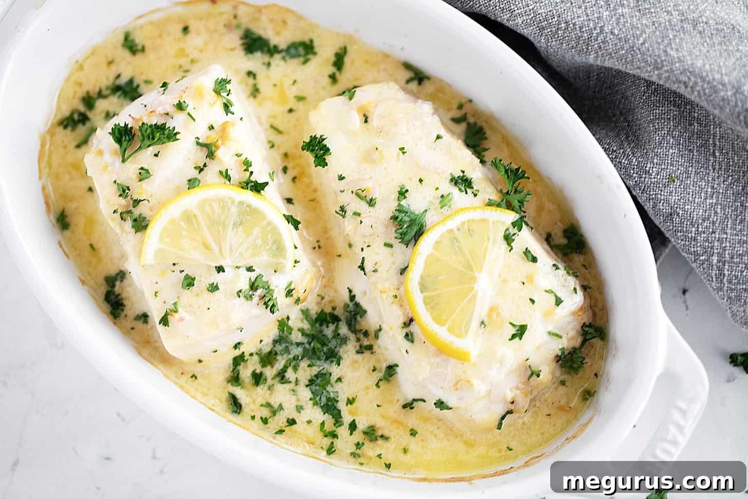 Creamy lemon baked halibut in the baking dish, garnished with fresh parsley.