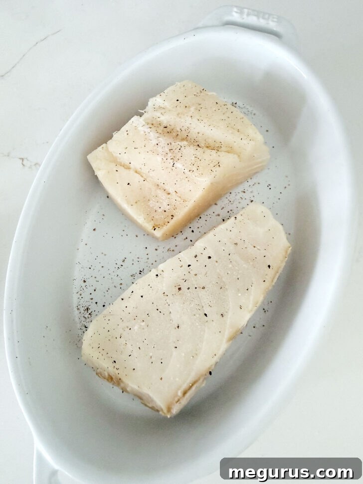 Halibut fillets seasoned and placed in a baking dish.