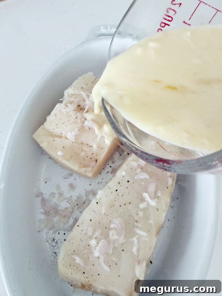 Pouring the creamy lemon sauce generously over the halibut and shallots.