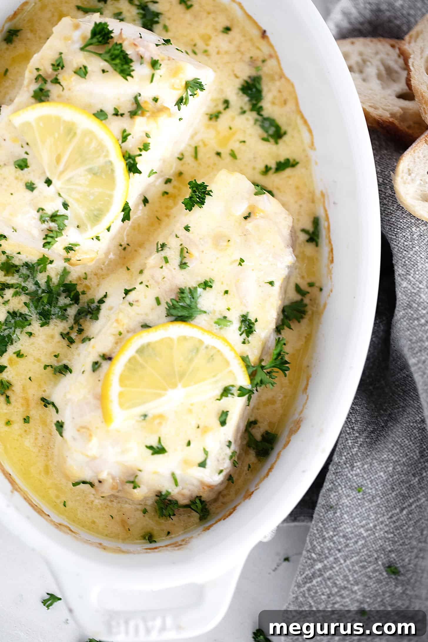 Creamy lemon baked halibut served in a rustic dish, garnished with fresh herbs.
