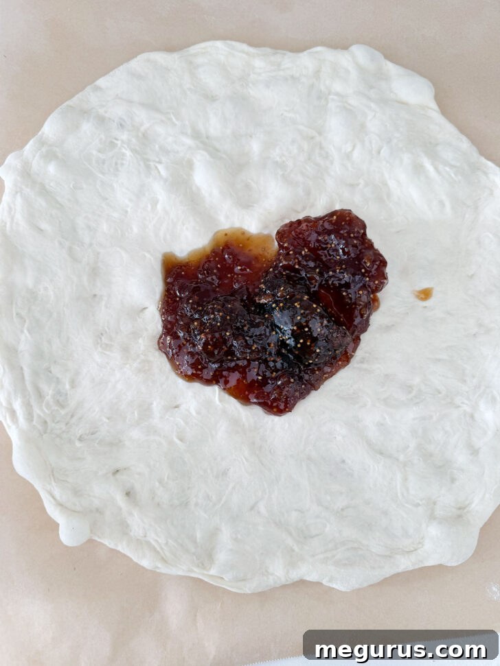 Fig jam spooned onto pizza dough, showing the first step of topping the pizza.