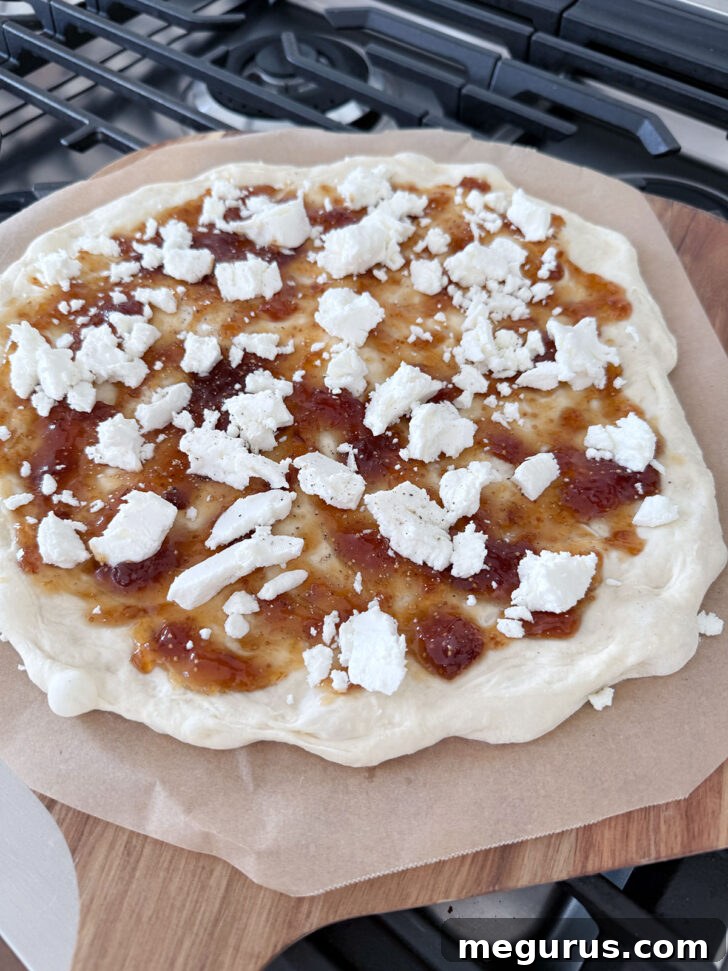 Fig jam and goat cheese on the pizza dough, ready for the oven, illustrating the second step.