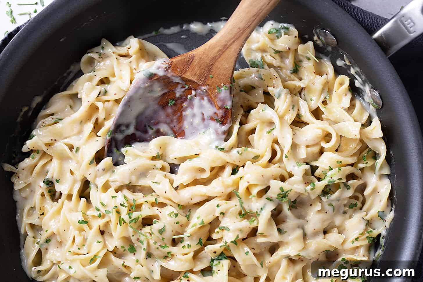 Creamy egg noodles simmering in a skillet with a wooden spoon.
