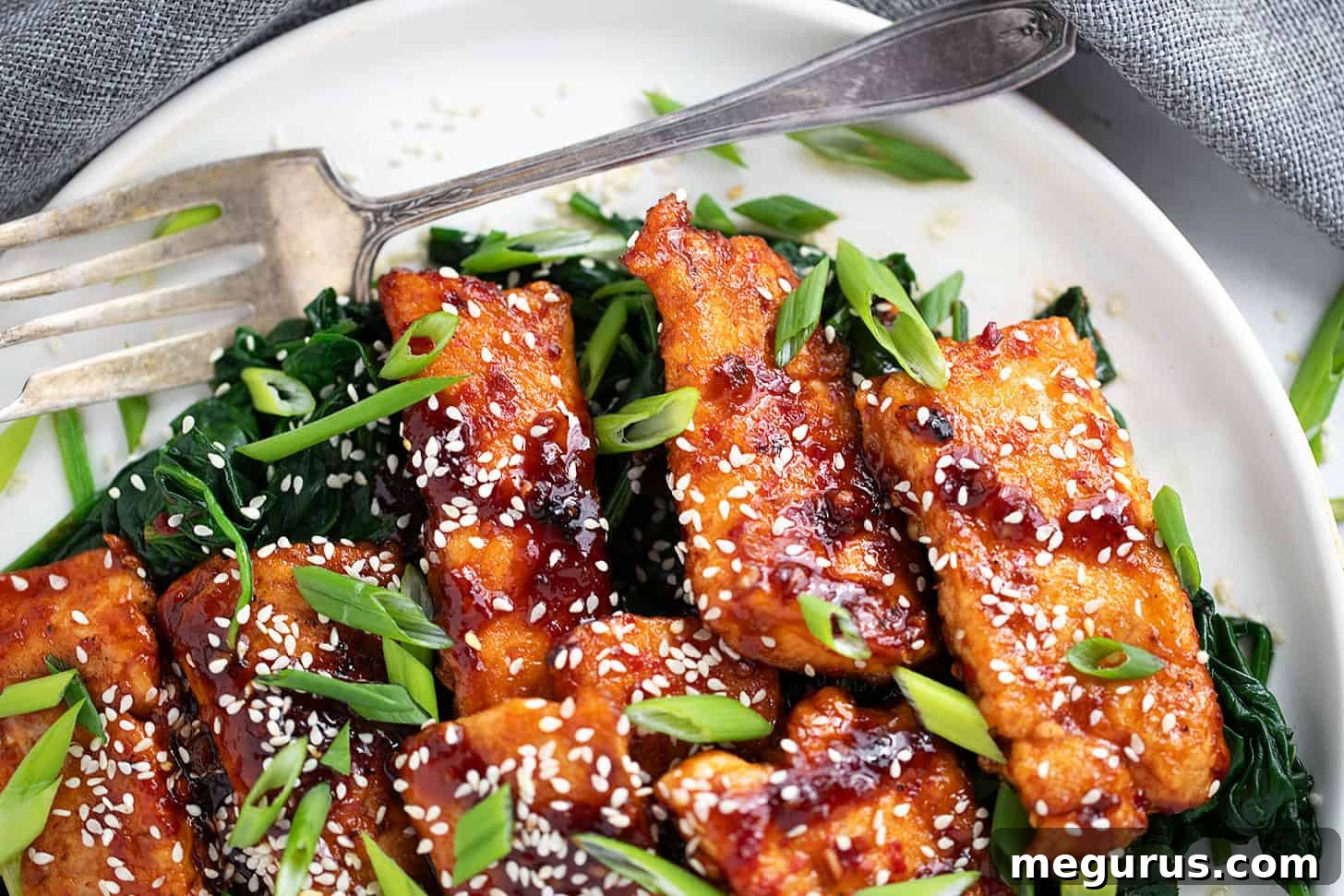 Sticky spicy salmon on a serving platter with cooked spinach.