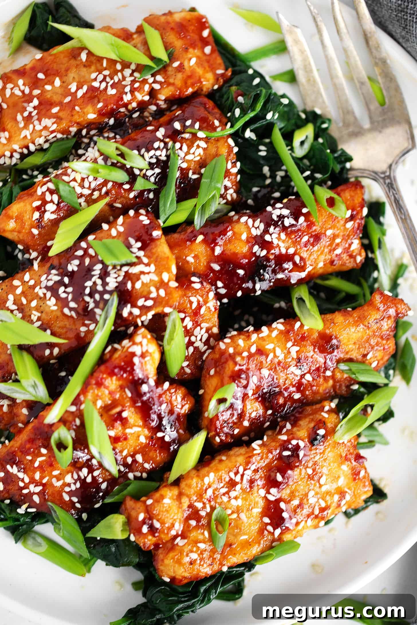 Sticky spicy salmon on a serving platter with cooked spinach.