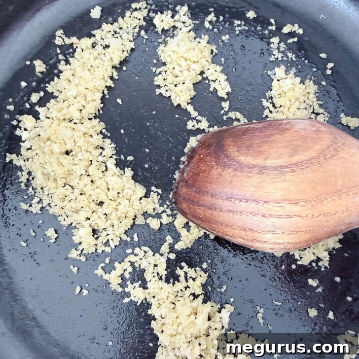 Panko cooking in a skillet with oil and garlic, beginning to brown.