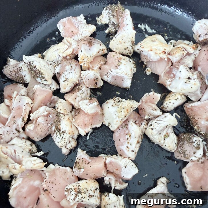 Chicken cooking with the spices in a skillet, turning golden brown.