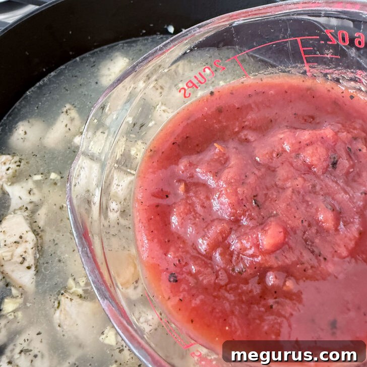 Adding the first portion of crushed tomatoes to the skillet with broth and chicken.