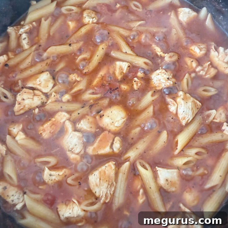 Penne pasta added to the skillet, submerged in the sauce.