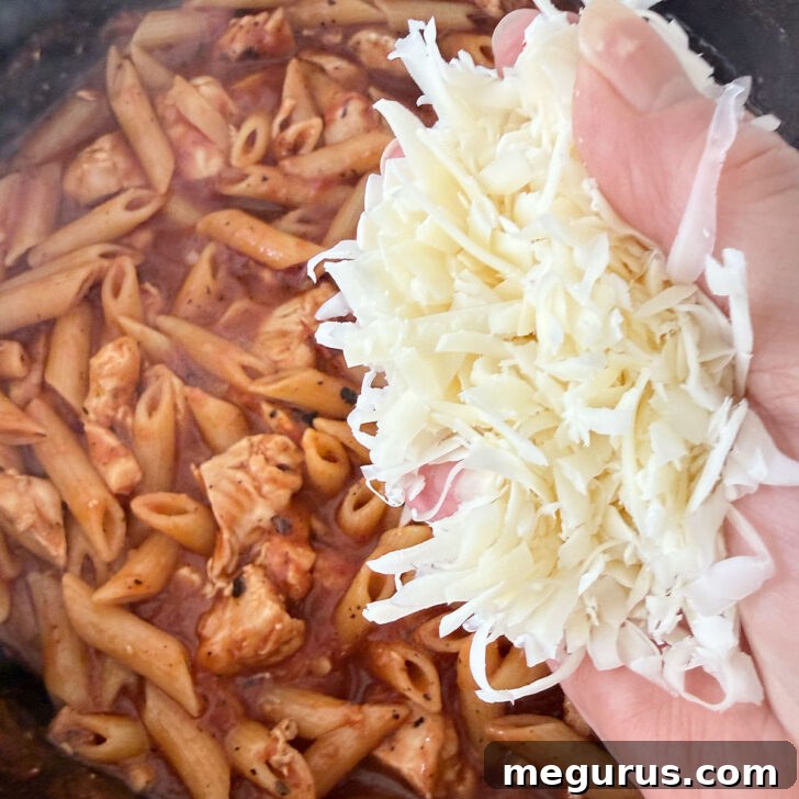Adding shredded mozzarella cheese to the top of the pasta for melting.