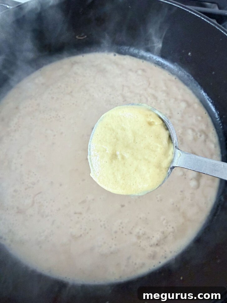 Dijon mustard being whisked into the creamy sauce in the skillet.