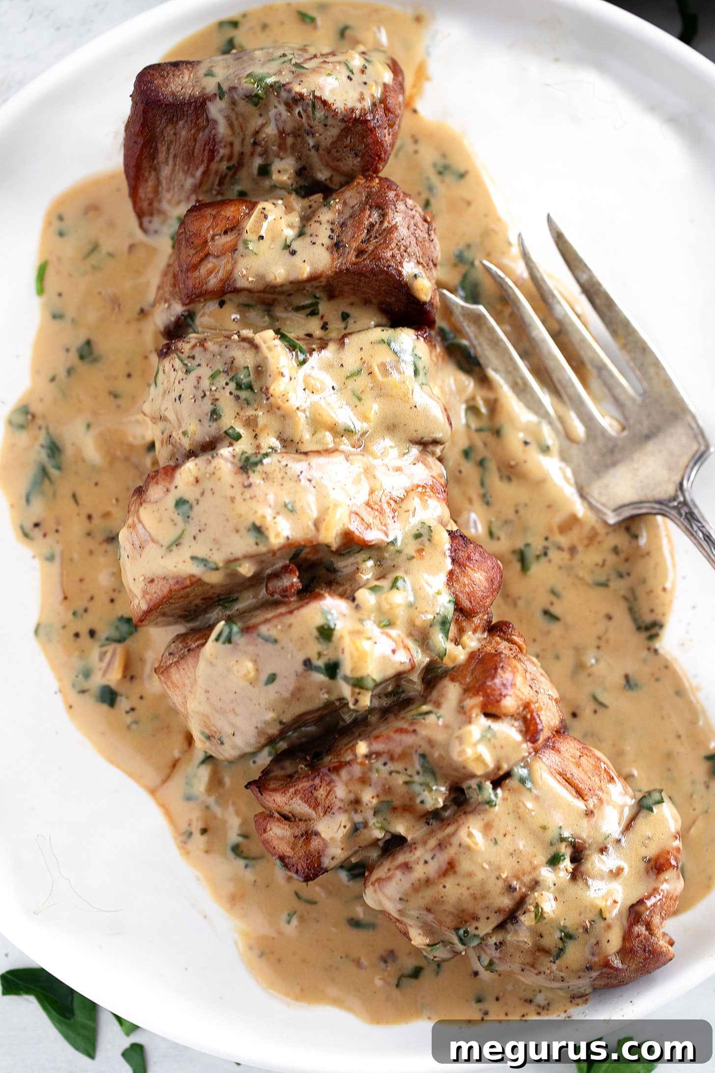 A close-up of a beautifully plated pork tenderloin medallion dinner, featuring seared pork and creamy Dijon sauce, garnished with fresh herbs.