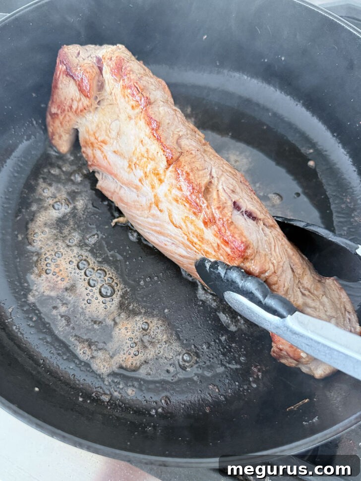 Pork tenderloin searing in a hot skillet, developing a golden crust.