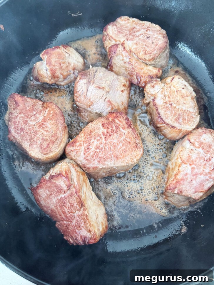 Individual pork medallions browning in a hot skillet, showing a beautiful crust.