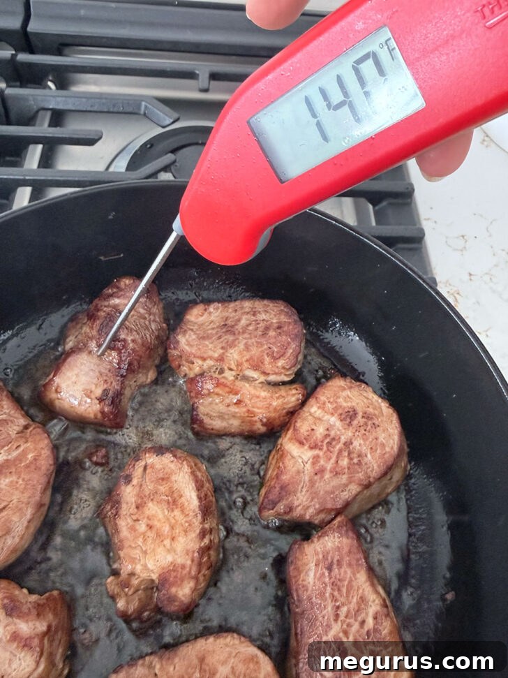 An instant-read thermometer being used to check the internal temperature of a pork medallion in a skillet.