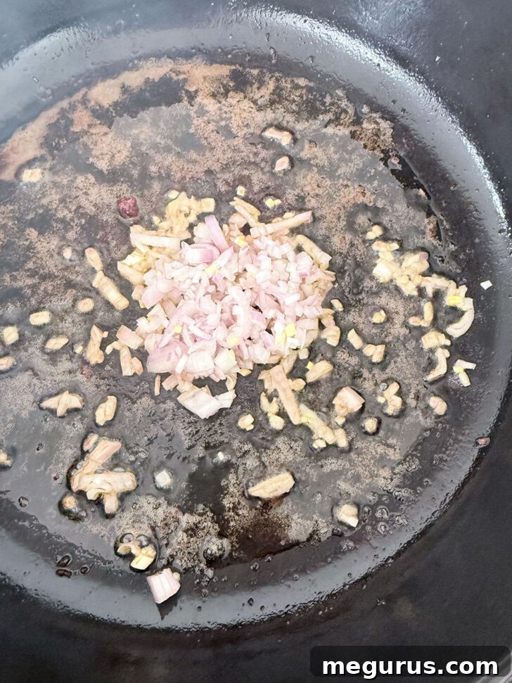 Diced shallots and garlic sizzling in the same skillet after the pork has been removed.