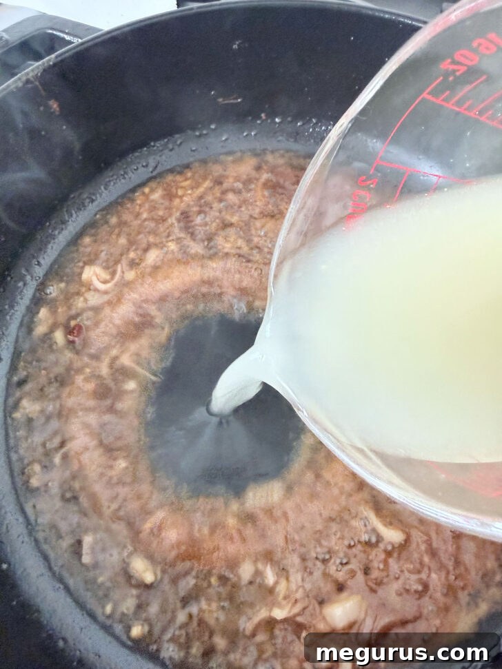 Chicken broth being poured into the skillet with the shallots and wine, beginning to form the sauce base.