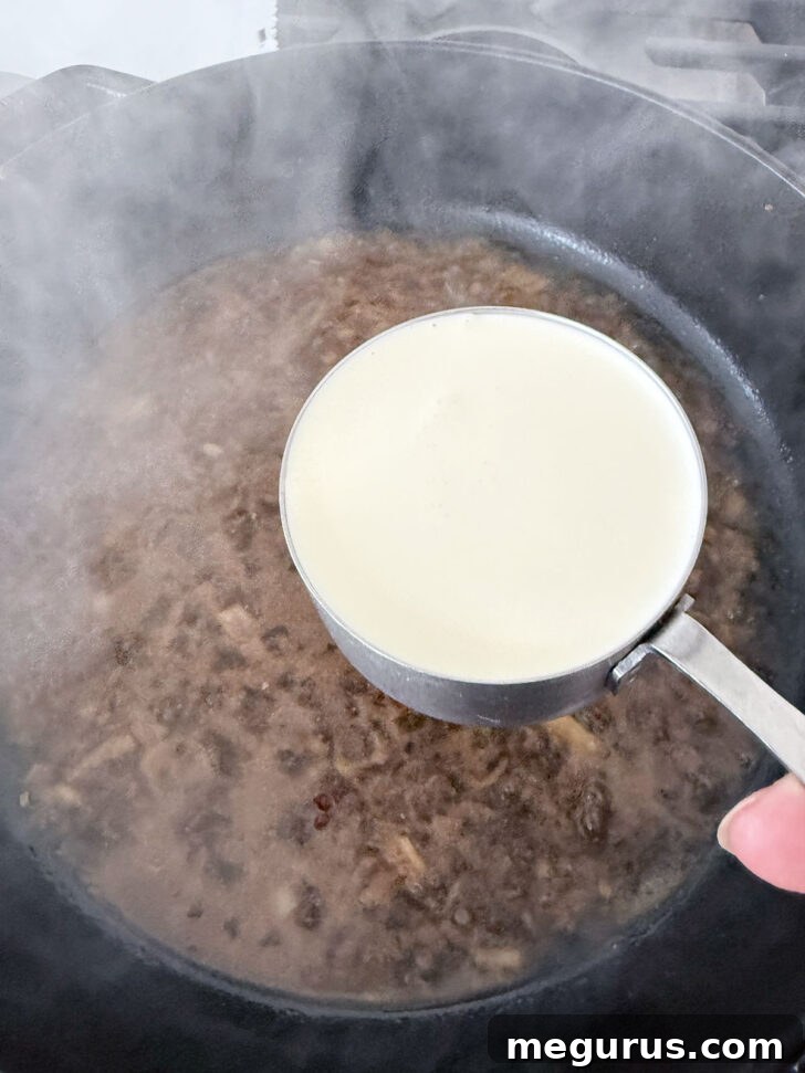 Heavy cream being stirred into the simmering sauce in the skillet.