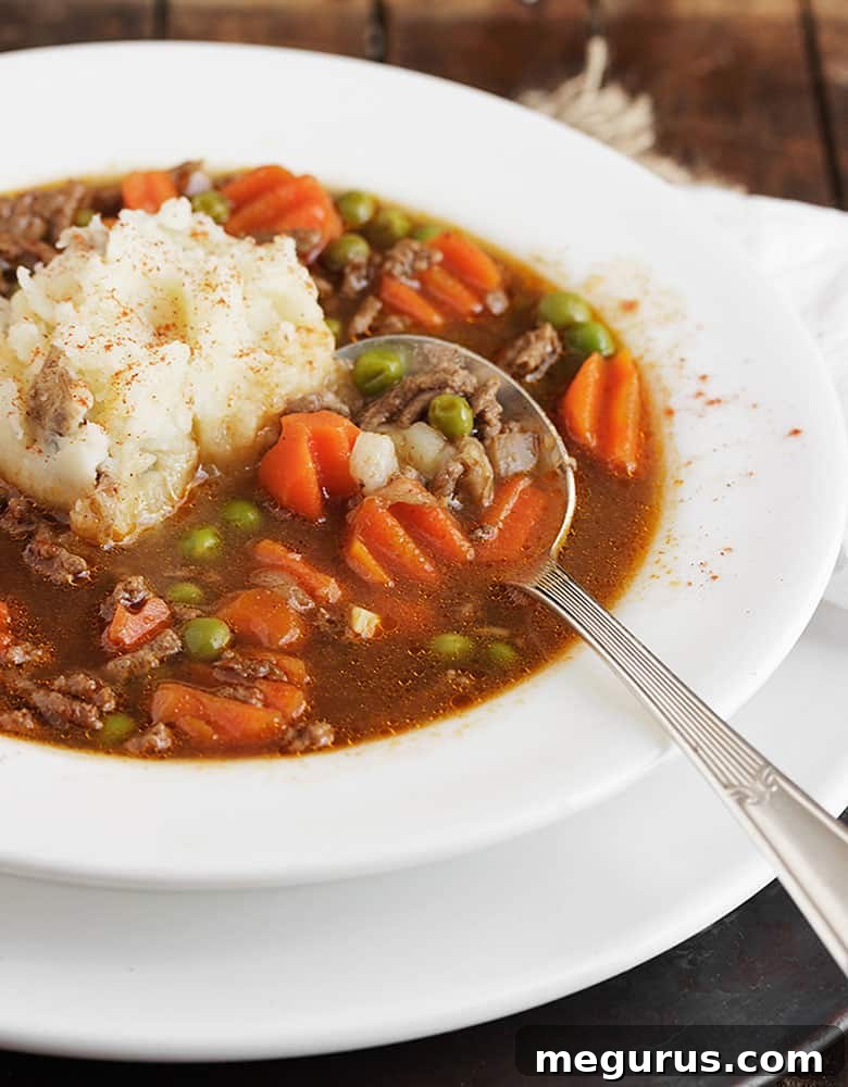 A top-down view of Shepherd's Pie Soup in a white bowl, garnished with fresh parsley and a dollop of mashed potatoes.