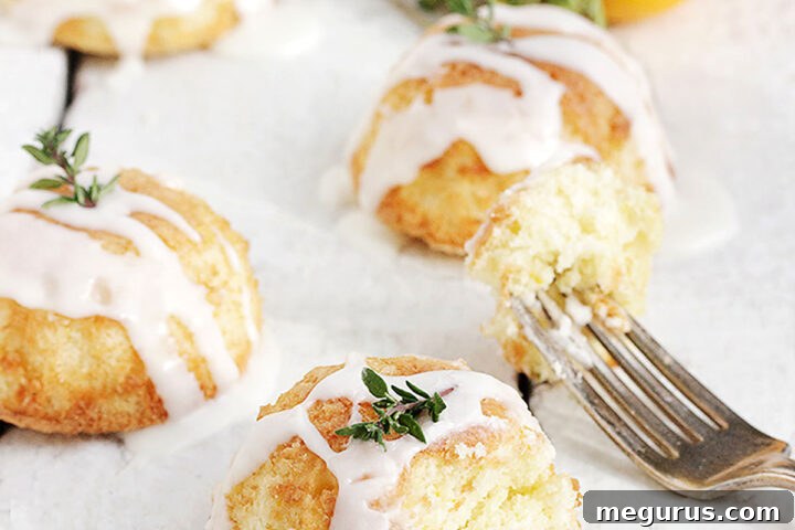 A beautifully arranged plate of glazed mini lemon thyme olive oil cakes with fresh lemon and thyme for garnish.