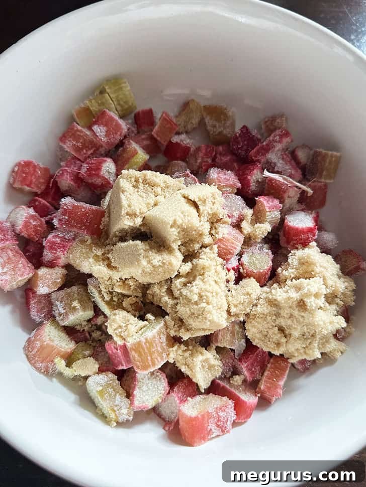 Frozen rhubarb and brown sugar being mixed in a bowl.