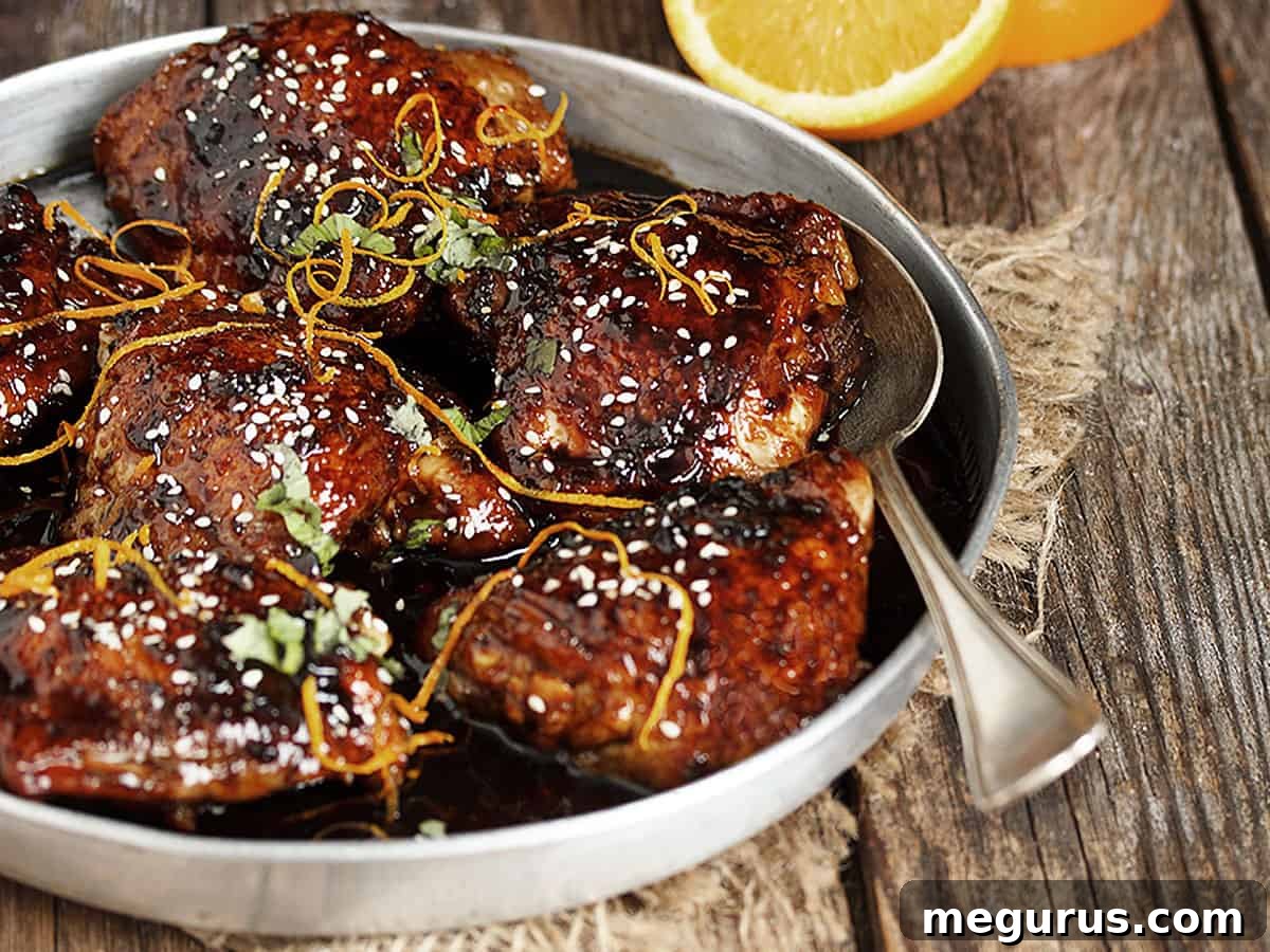 Serving bowl filled with perfectly glazed Asian sticky chicken, garnished with green onions and sesame seeds, ready to eat.