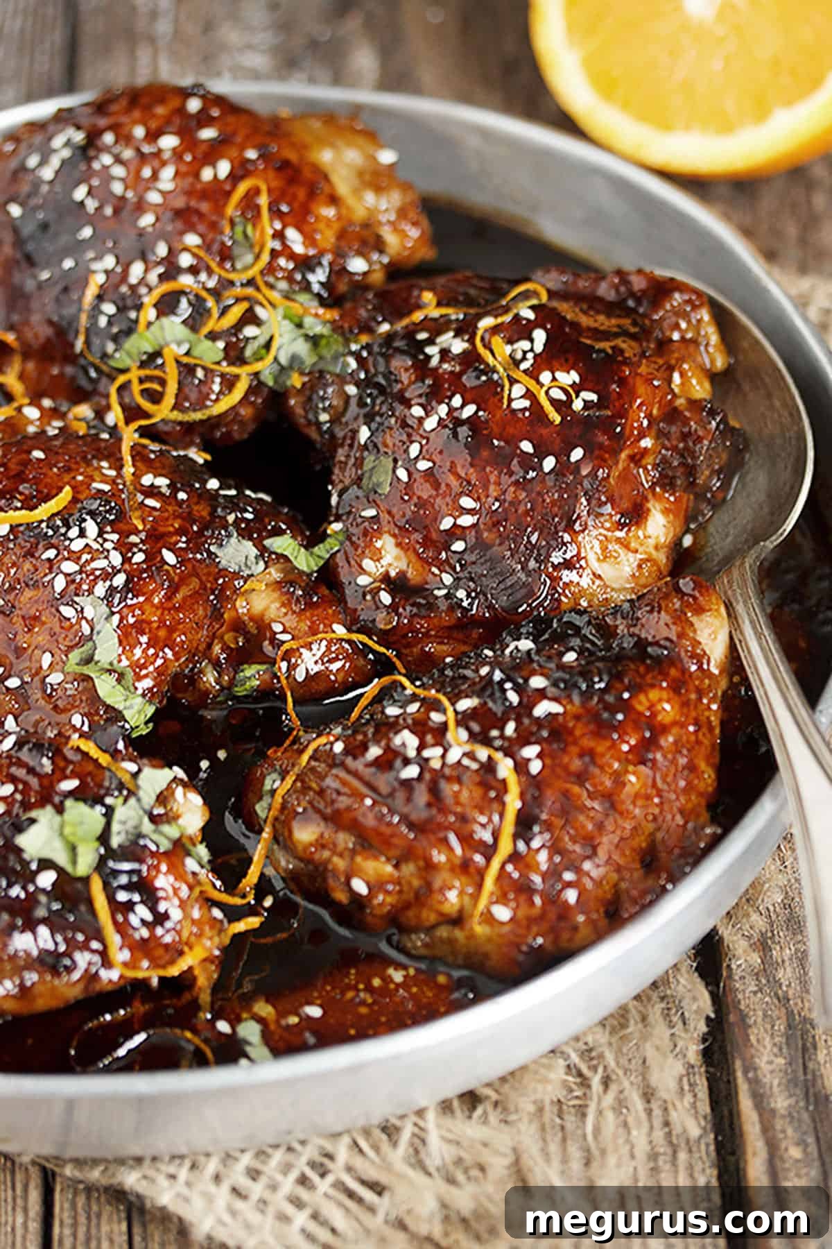 Fresh ingredients for Asian sticky chicken laid out on a cutting board, including chicken thighs, chili garlic sauce, and oranges.