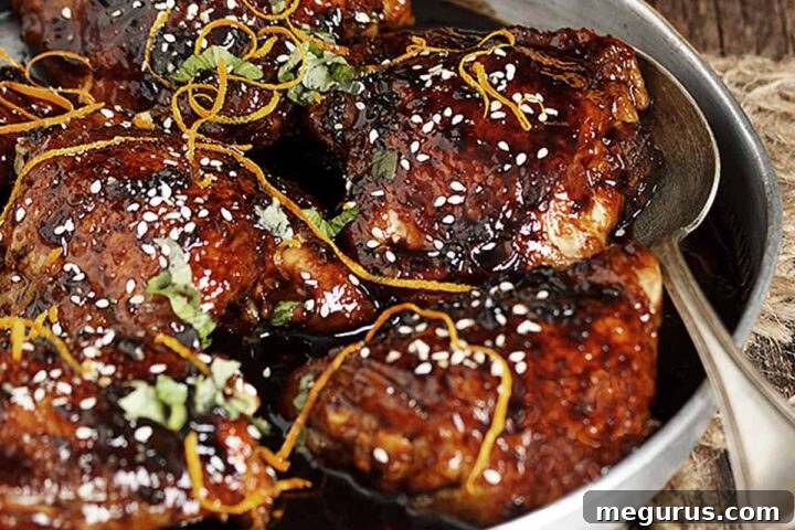 Close-up of Asian sticky chicken in a serving bowl, showcasing the glossy glaze and garnishes.