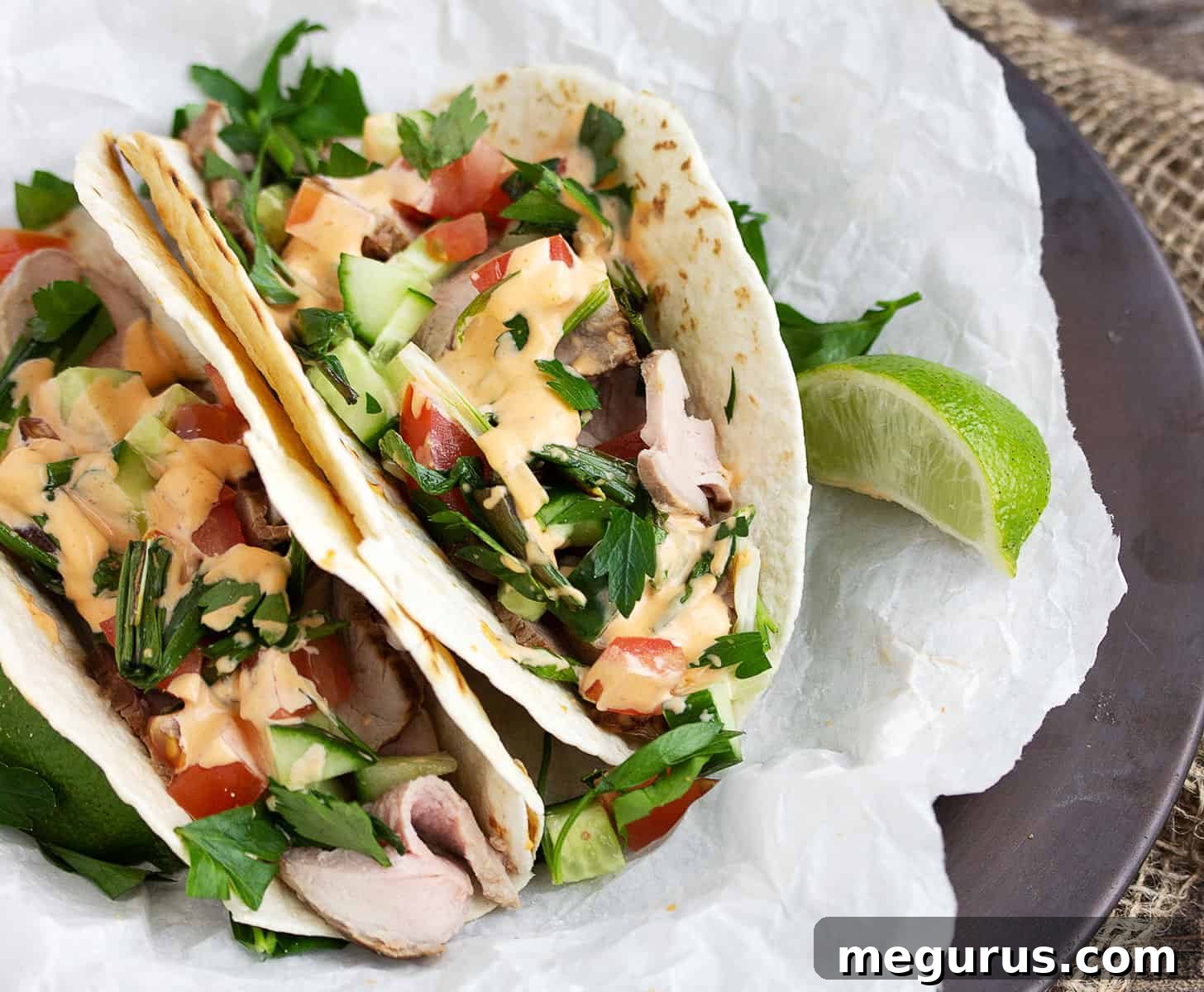 Flavorful Asian-inspired pork tacos arranged on parchment paper, showcasing tenderloin, sriracha mayo, and fresh toppings.