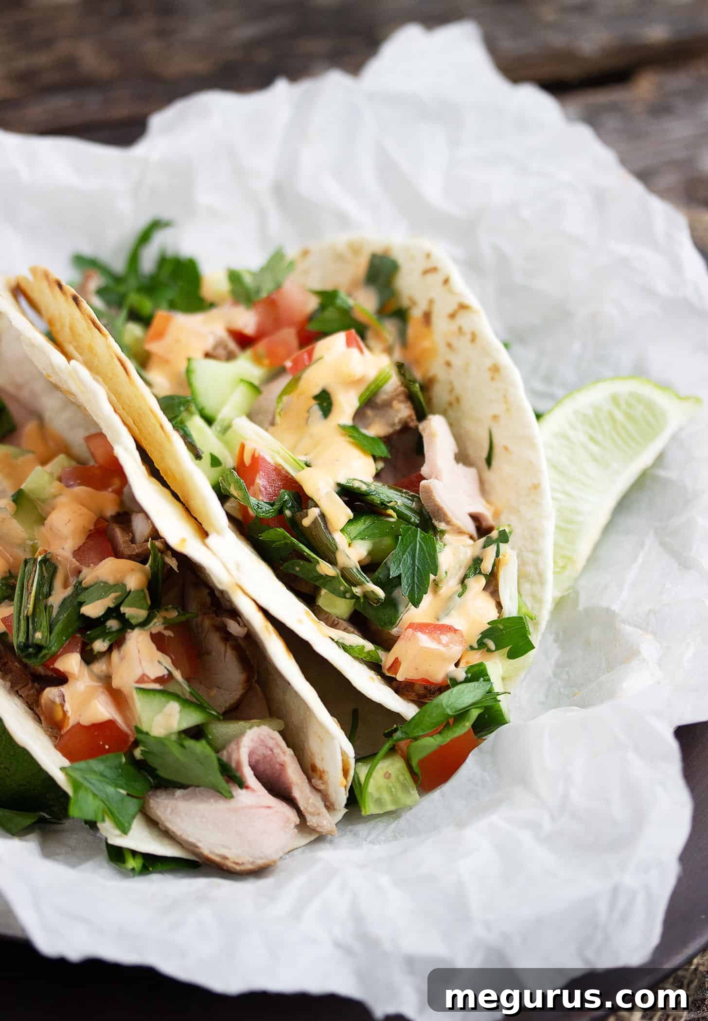 Two Asian inspired pork tacos placed on parchment paper, ready to be served.