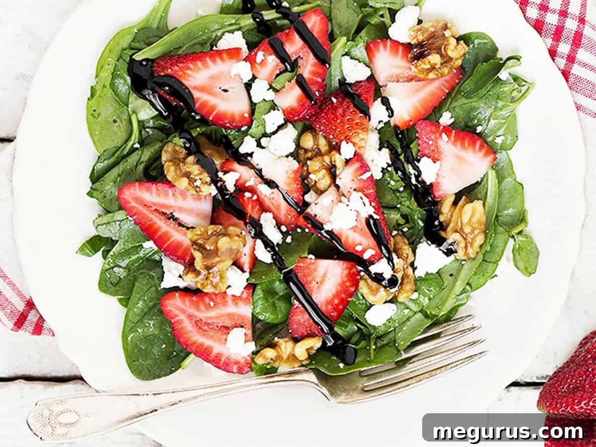A beautifully presented spinach strawberry salad with goat cheese and maple glazed walnuts on a white plate, garnished with balsamic glaze.