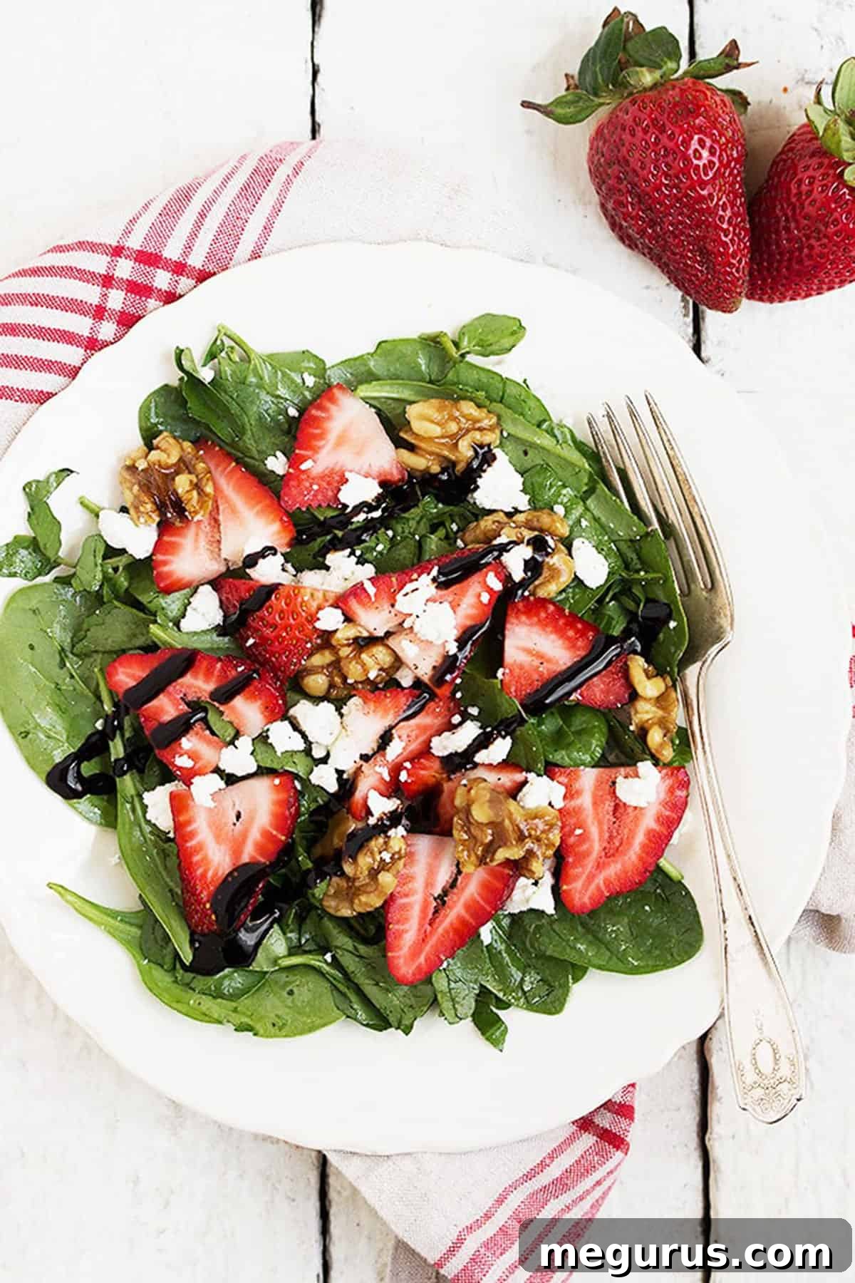 Close-up of a fresh spinach strawberry salad with vivid red strawberries, creamy goat cheese, and crunchy maple glazed walnuts.