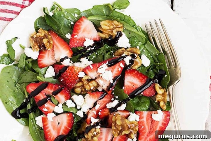 Strawberry Spinach Salad on a white plate with goat cheese and maple glazed walnuts.
