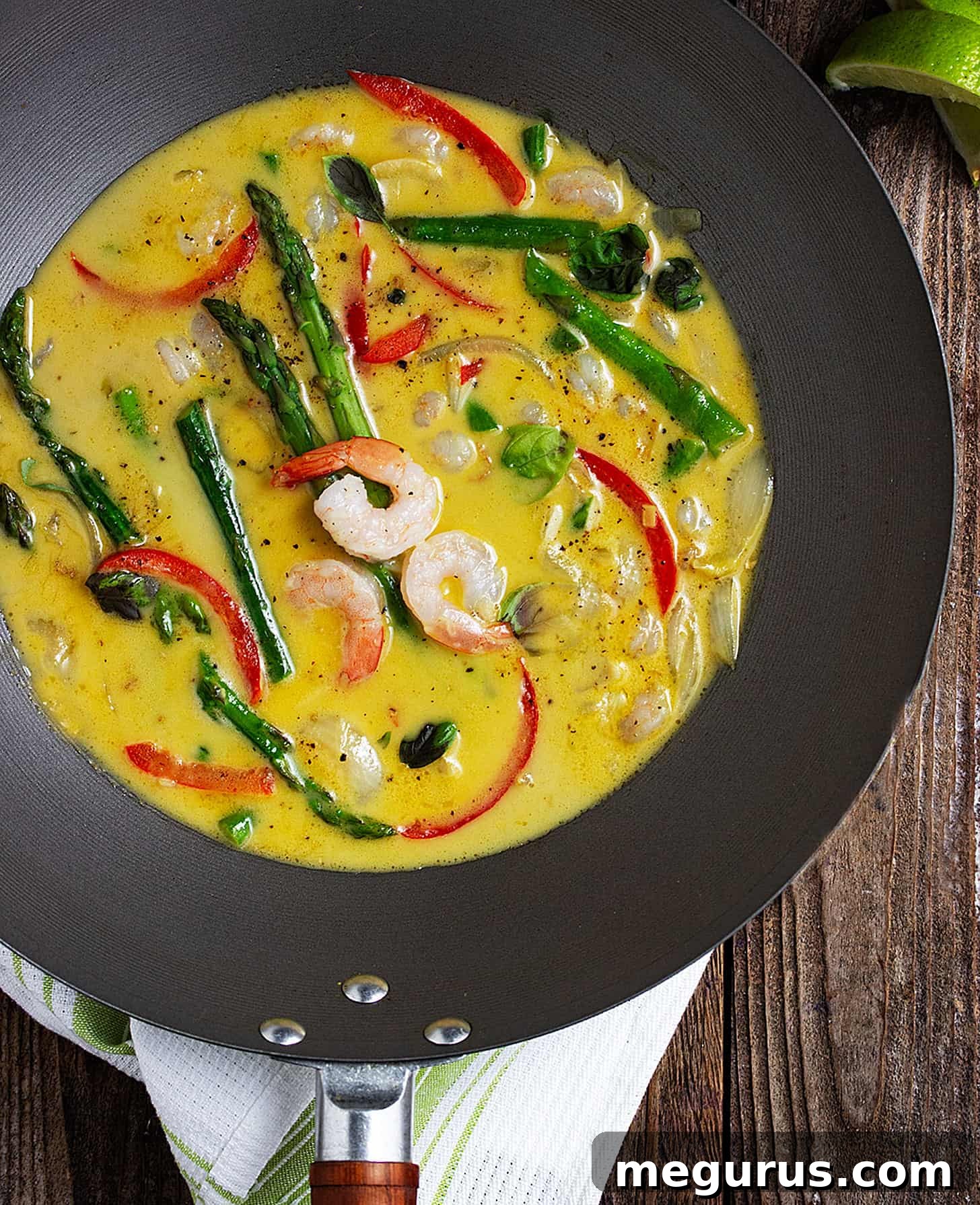 Close-up of fresh ingredients for Thai green curry shrimp: shrimp, asparagus, curry paste, and lime