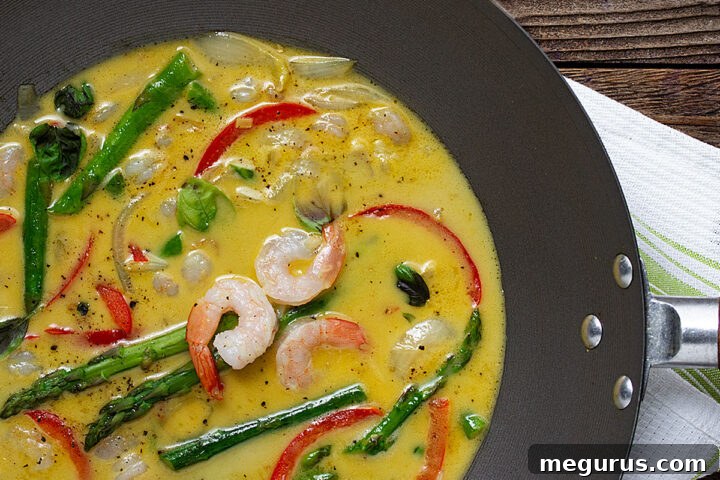 A serving of Thai green curry shrimp with asparagus in a bowl, garnished with basil