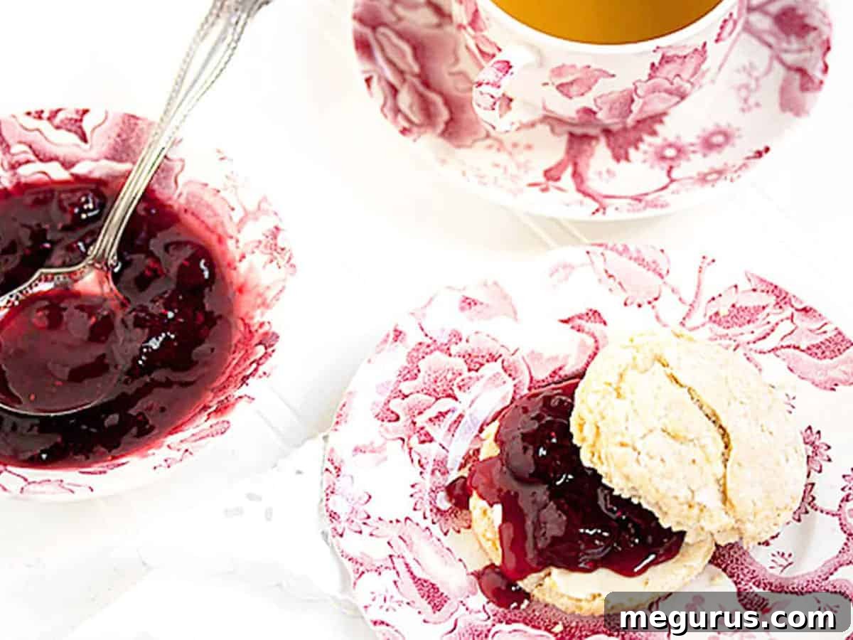 Homemade strawberry balsamic black pepper jam served beautifully on a freshly baked scone, highlighting its rich ruby-red color and inviting texture.