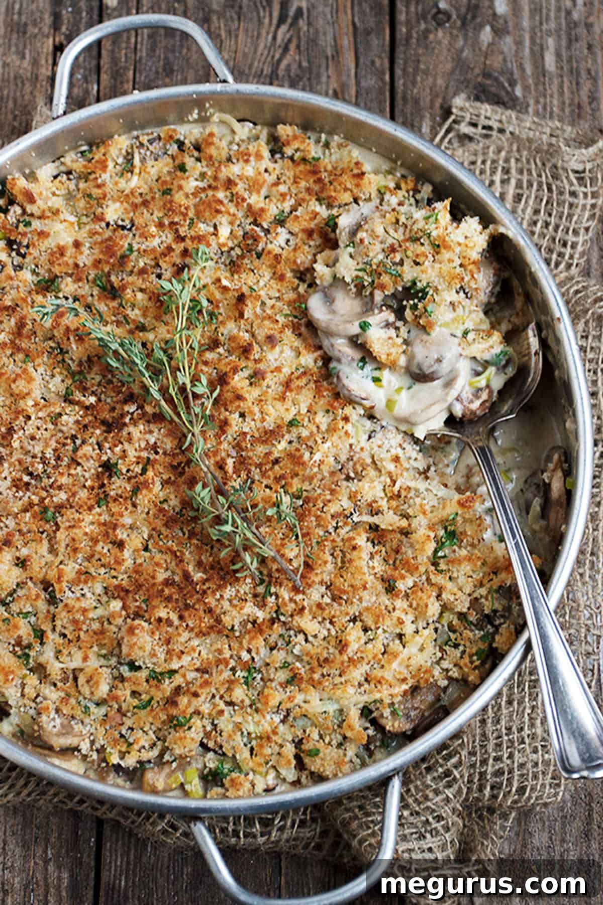 Close-up of creamy mushroom and leek bake in a white baking dish with a spoon, showing the crispy topping