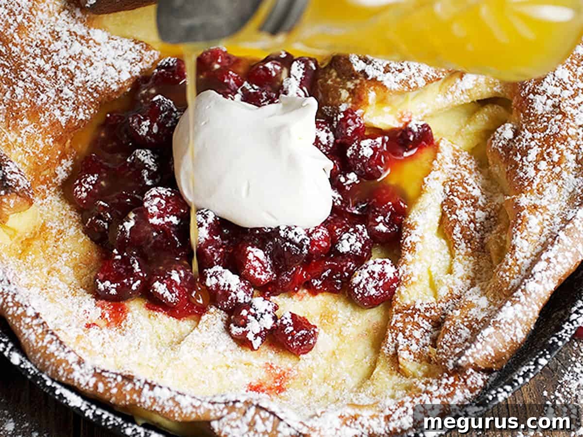 Puffy Cranberry Dutch Baby pancake drizzled with clementine orange syrup, ready for serving.