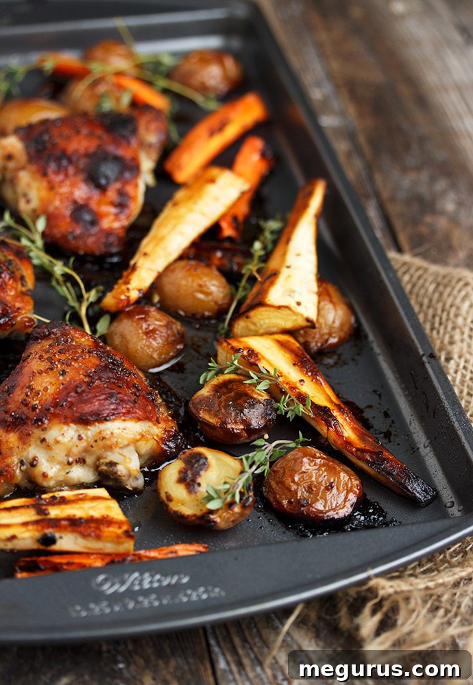 Close-up of golden-brown Sheet Pan Honey Mustard Chicken thighs with perfectly roasted carrots, parsnips, and potatoes