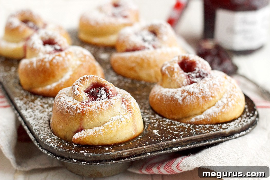 Freshly baked Raspberry Jam Rose Buns arranged beautifully in a muffin tin, showcasing their intricate, rose-like shape and golden-brown crust.