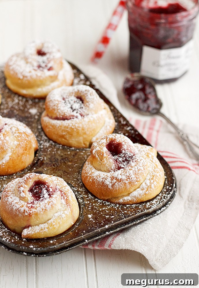 Close-up of a single Raspberry Jam Rose Bun, perfectly golden with visible jam filling peeking through its layers, ready to be enjoyed.