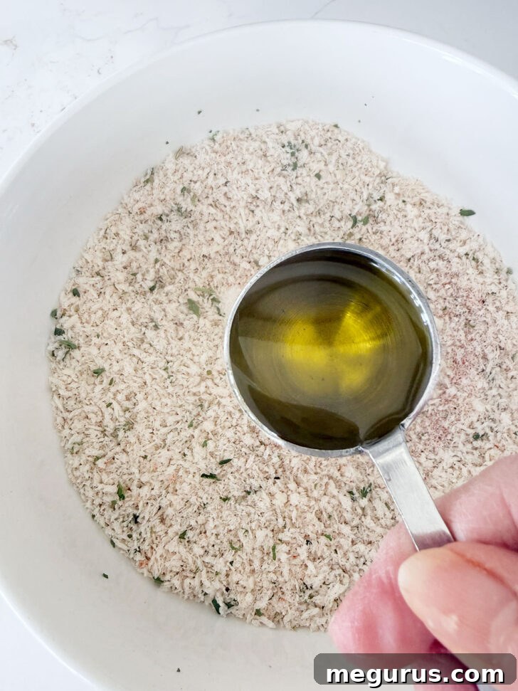 Olive oil being drizzled into the panko breading mixture in a bowl.