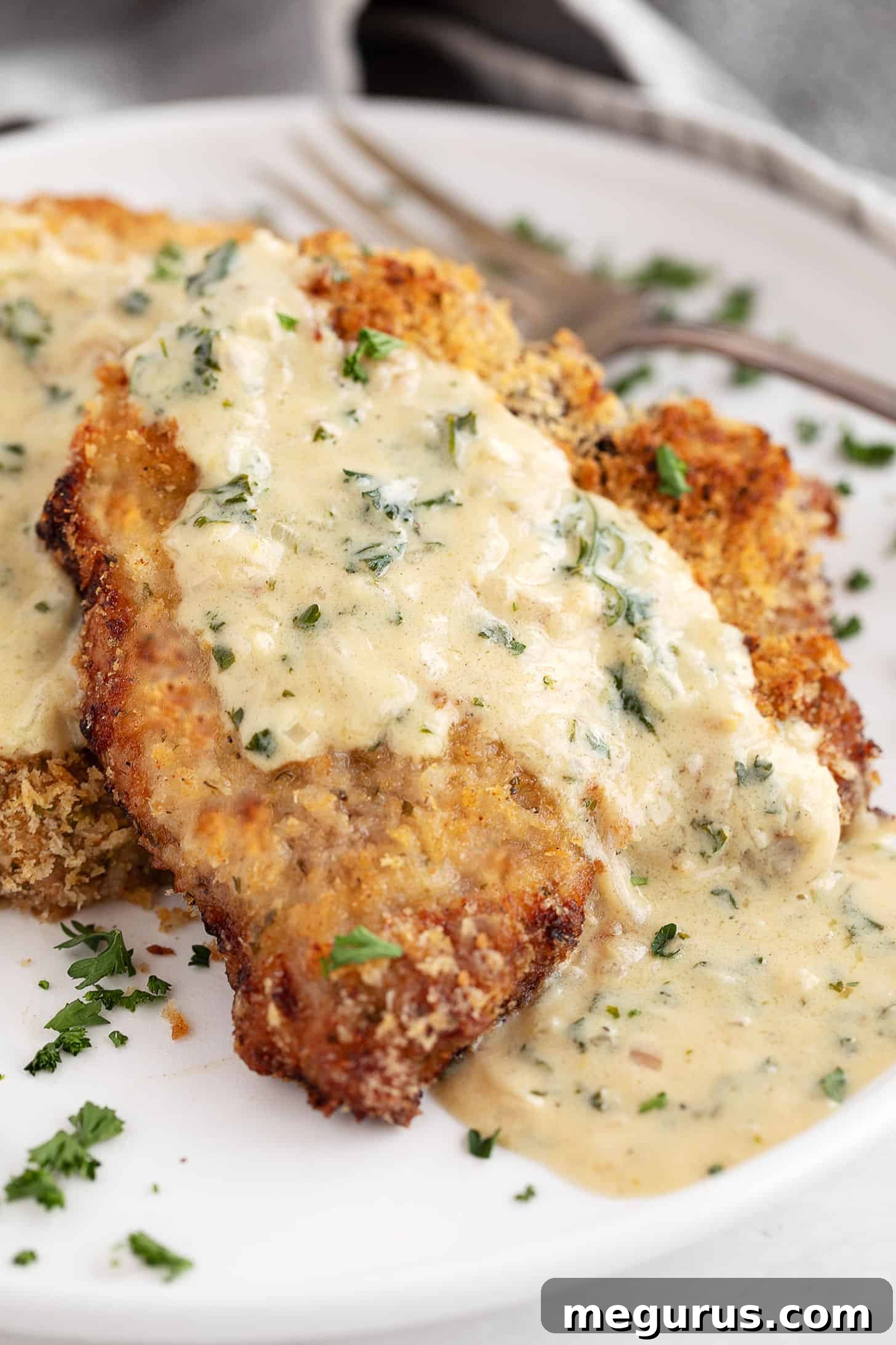 Close-up of a single oven-baked panko breaded pork chop with creamy mustard sauce and fresh parsley garnish.